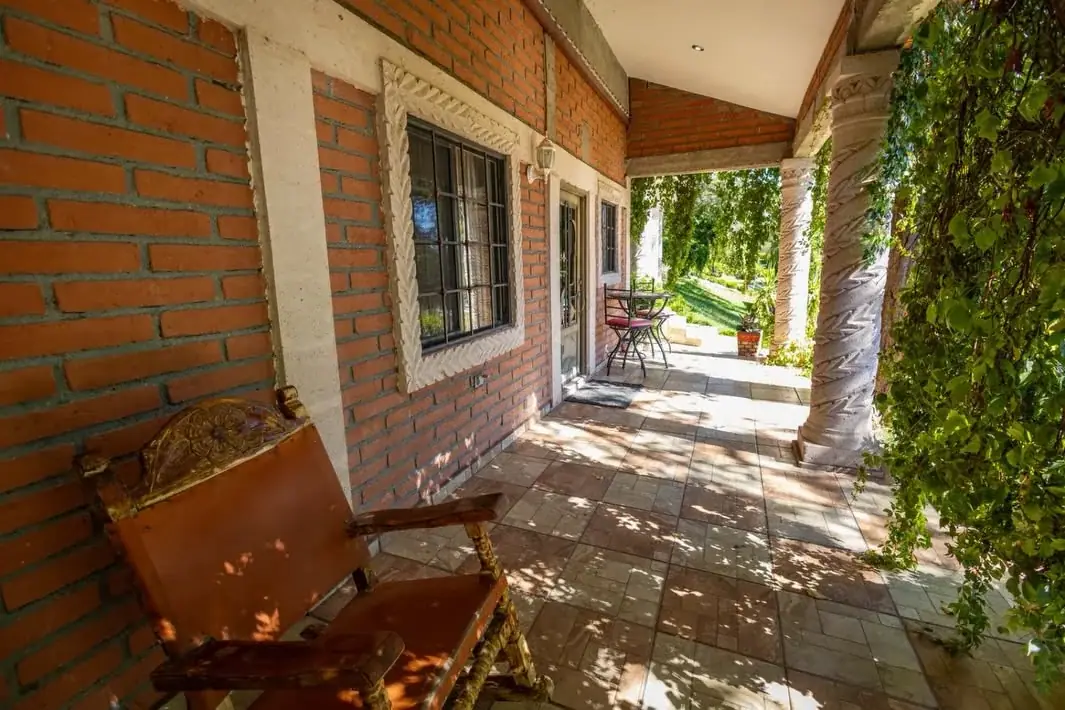 Corredor de ladrillo con un sillón de madera y cuero, abierto al jardín