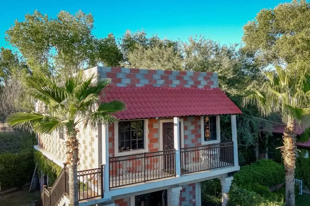 Casa de dos plantas con techo de teja roja y balcones, entre palmas